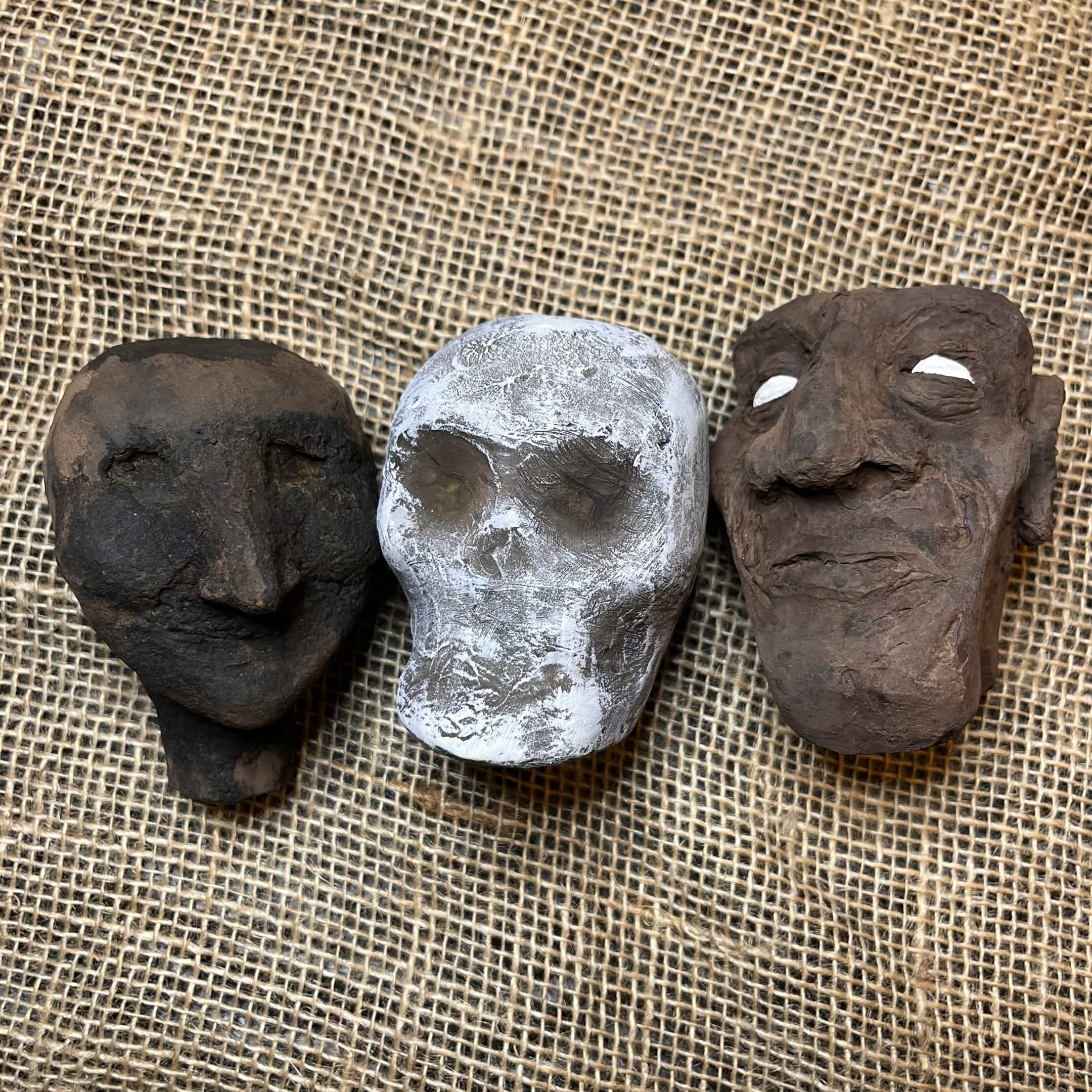 photo of 3 paper mache puppet heads on top of a piece of burlap